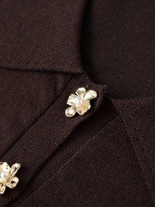 Close-up of golden flower button with white pearl on a dark brown knit top neck