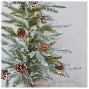 Close-up of a tabletop flocked Christmas tree with pine cones and warm LED lights