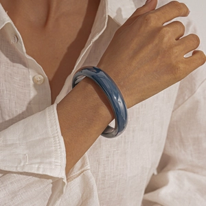 Close-up of polished dark blue resin round bangle on a linen sleeve for a minimalist look