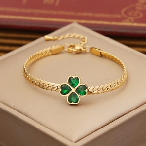 Golden clover bracelet with emerald heart stones on beige jewelry box display