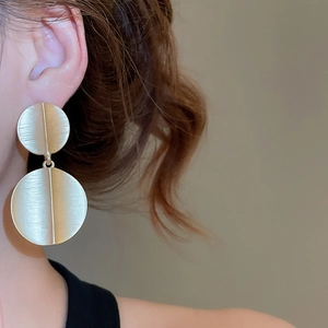 Detail of gold brushed metal double disc earrings showing modern minimalist texture