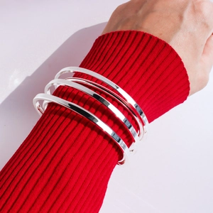 Set of four polished silver metal bangles worn over a stylish red knitted sweater sleeve