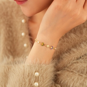 Gros plan d'un bracelet vintage doré avec breloques en émail coloré sur manche en maille