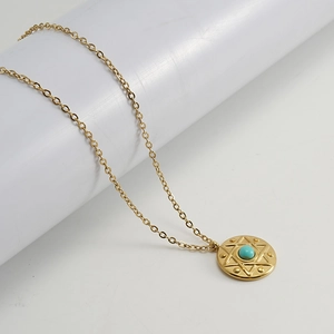 Detail of gold necklace with round turquoise pendant featuring a star pattern and dots