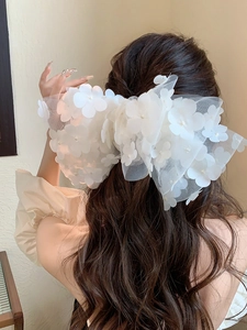 Detail of oversized white mesh bow hair clip with floral accents and pearls on model