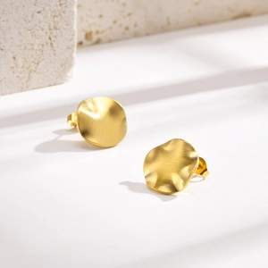 Detailed close-up of matte gold irregular brushed metal earrings on a stone background
