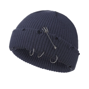 Detailed view of dark blue knit beanie with metal pins, rings and distressed ripped texture