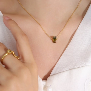 Collier doré élégant avec pendentif en cristal vert rectangulaire porté par un mannequin