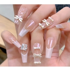 Detail of nude pink press-on nails with white French tips, bows, pearls and large rhinestone