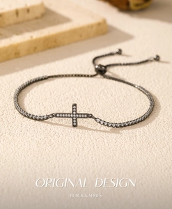Detail of adjustable black chain bracelet with a sparkling zircon cross on a textured stone