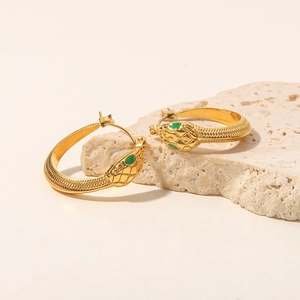Detail of golden snake hoop earrings with green crystal eyes on a natural stone base