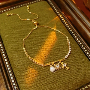 Macro view of adjustable gold zircon bracelet with pearl, starburst, and cross charms