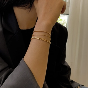 Detail of three stacked gold snake and link chains on a black suit sleeve background
