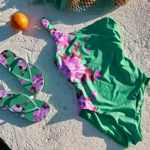 Floral print bikini set with matching flip-flops and orange accents on beach sand