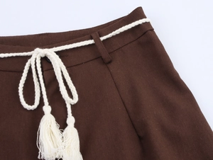 Detail of deep brown linen trousers featuring a white braided rope belt with fringe tassels