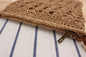 Detail of woven straw handbag featuring hollow knit texture and brown zipper closure