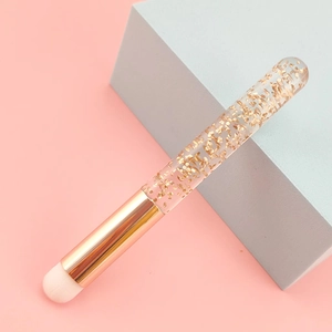 Detail of round concealer brush with gold foil transparent handle on geometric background