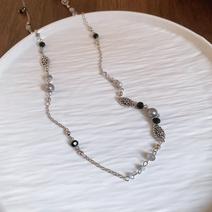 Detail of silver long necklace with grey pearls and hollow flower metal spacers on white tray