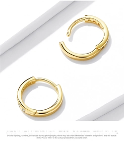 Detail of gold huggie earrings with three zircons on a white geometric stage