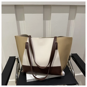 Dettaglio di una borsa tote tricolore beige e caffè scuro su una sedia nera