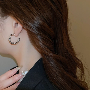 Close-up of textured silver C-shape earrings worn by a model in a minimalist style