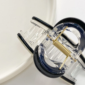 Minimalist clear hair claw clip with black trim and gold spring on a white surface