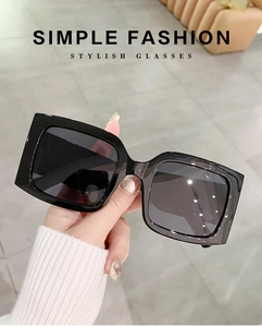 Detail of hand-held square oversized sunglasses in glossy black with dark lenses