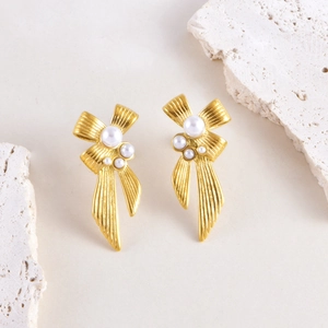 Elegant gold bow earrings with faux pearls on vintage white stone display for women