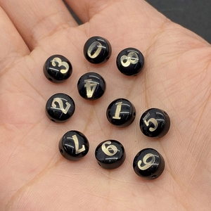 Dettaglio macro di perline nere da 8 mm con numeri dorati per gioielli fai-da-te