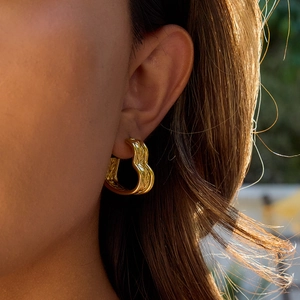 Close-up of 18K gold-plated stainless steel heart earring with woven texture on ear