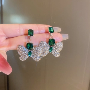 Close-up of silver butterfly earrings with green emerald square gems and tiny crystals
