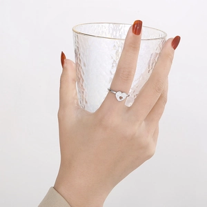 Silver open heart ring with micro-pave crystals on hand holding a clear glass