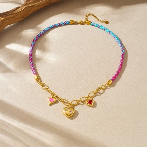 Collier cœur tressé fait main avec chaîne dorée et strass colorés sur fond de sable