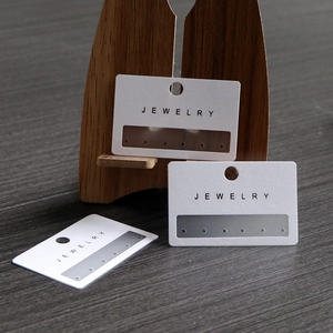 White PVC jewelry display card with six holes for earrings on a wooden stand