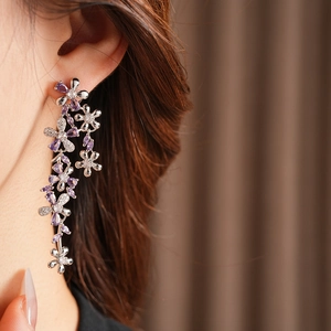 Close-up of dangling silver flower earrings with purple zircons worn by a model