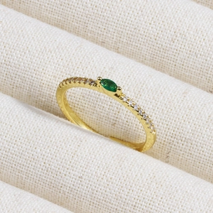 Macro shot of gold ring with emerald marquise stone and zircon on textured fabric