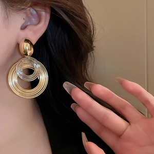 Detail view of multi-layered golden geometric hoop earrings worn by a model