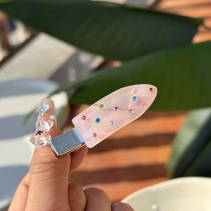 Handheld pink translucent resin duckbill hair clip with colorful rhinestones outdoors