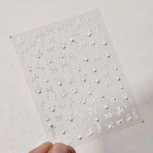 Detail of 3D embossed nail art stickers featuring white crystal bows and butterfly designs