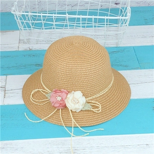 Détail d'un chapeau de paille pour enfant avec fleurs décoratives en tissu rose et blanc