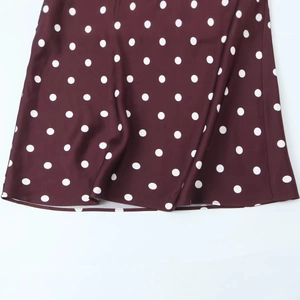 Elegant burgundy polka dot dress featuring a fluid draped hem and silky fabric texture