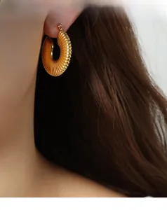 Detail shot of chunky gold hoop earrings with croissant textured design on female model