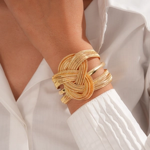 Close-up of chunky gold woven knot cuff bracelet with metallic tube texture and shine