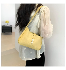 Detail of a chic yellow suede shoulder bag with a simple metal clasp worn by a model