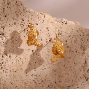 Detailed close-up of gold knotted stud earrings on a textured beige stone background