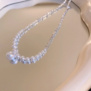Detail showing elegant white pearl pendant and textured silver link chain on a vanity tray