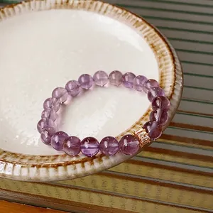 Purple amethyst beaded bracelet with gold crystal charm on textured ceramic plate