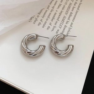 Detail view of silver C-shaped twisted hoop earrings on a clean minimalist background