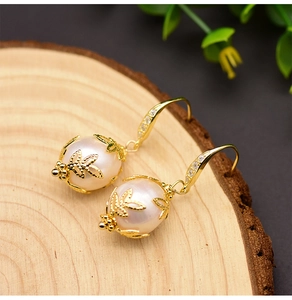 Macro view of baroque pearl earrings with gold leaf detail and zircon inlay on wood