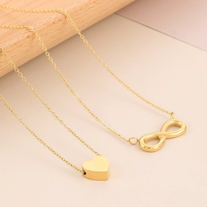 Detail of gold-plated infinity symbol and heart pendant necklaces on soft pink background